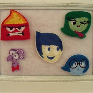 May include: Five felt patches depicting characters from the movie Inside Out. The characters are Joy, Sadness, Anger, Disgust, and Fear. The patches are all different colors and have different facial expressions.