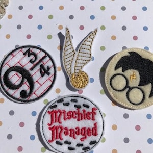 May include: Four embroidered iron-on patches featuring Harry Potter themes. The patches are white with black and red embroidery. The patches include a lightning bolt, a snitch, a house crest, and the words "Mischief Managed".