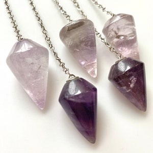 May include: Four amethyst crystal pendulums with silver chains. The pendulums are different shades of purple and pink.