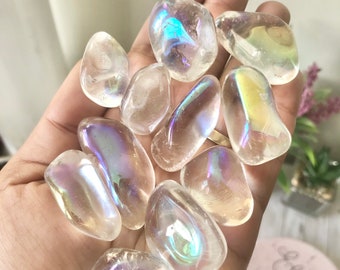 May include: A collection of iridescent clear quartz tumbled stones. The stones are smooth and have a rainbow sheen.