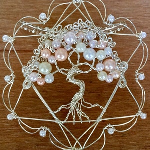 May include: A silver wire tree of life sculpture with pink, white, and cream colored beads. The tree is surrounded by a silver wire frame in the shape of a star of David.