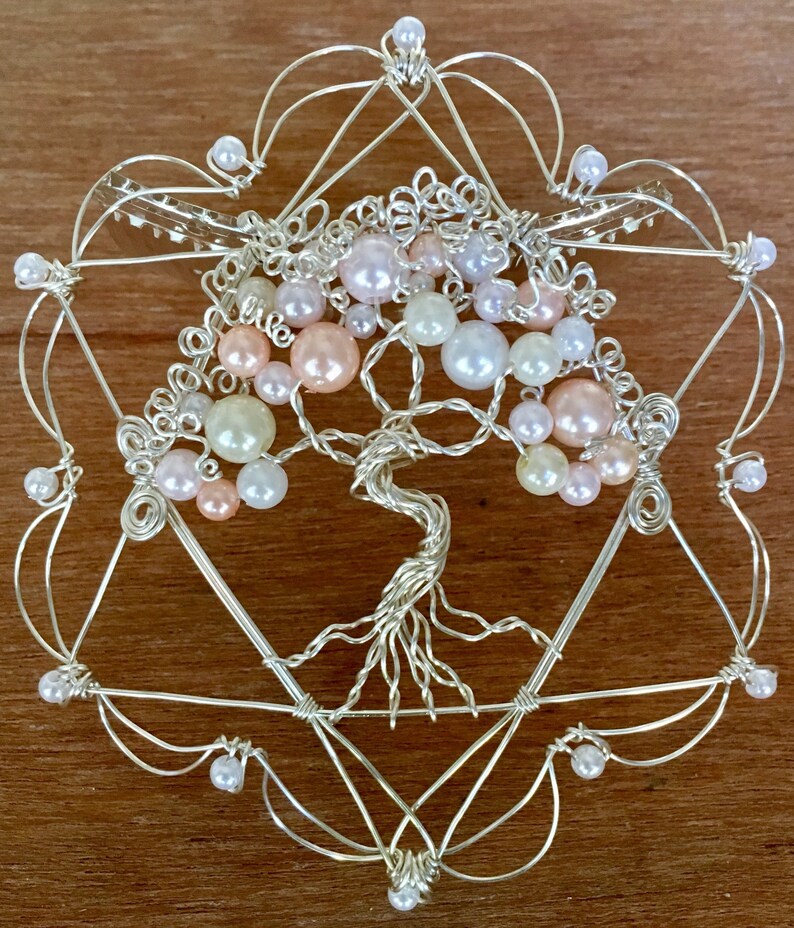 May include: A silver wire tree of life sculpture with pink, white, and cream colored beads. The tree is surrounded by a silver wire frame in the shape of a star of David.