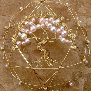 May include: A gold wire tree of life with pink and white pearl beads. The tree is surrounded by a gold wire circle with a star of David design.