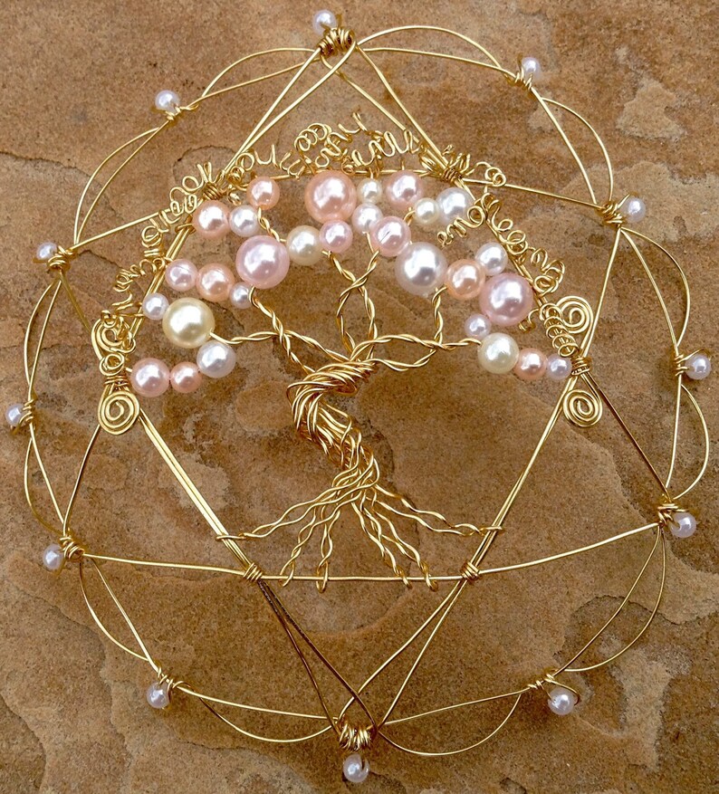 May include: A gold wire tree of life with pink and white pearl beads. The tree is surrounded by a gold wire circle with a star of David design.