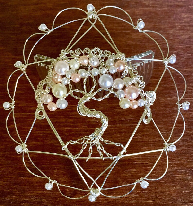 May include: A silver wire tree of life hair comb with pink and white pearls. The comb is set in a silver wire circle with a geometric design.