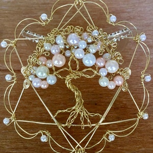 May include: A gold wire tree of life sculpture with pink, white, and cream pearls. The tree is surrounded by a gold wire frame in the shape of a star of David.