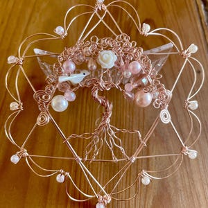 May include: A rose gold wire tree of life sculpture with pink and white beads and a white bird. The tree is surrounded by a rose gold wire heart shape.