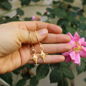 May include: A pair of gold hoop earrings with a star-shaped pendant. The pendant has a small circle in the center and four points.