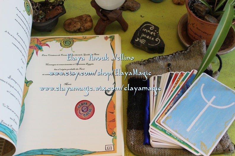 May include: A book with a certificate of formation for Elaya Anouk Wellino, a business that creates handmade items. The book is open to a page with the text "www.etsy.com/shop/ElayaMagic" and "www.elayamagic.wix.com/elayamagic". A deck of tarot cards is in a knitted bag.