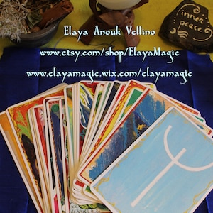 May include: A deck of tarot cards with colorful illustrations and gold trim. The cards are fanned out on a blue surface. The top card shows a white symbol on a blue background. The text "inner peace" is written on a black stone in the background. The text "Elaya Anouk Vellino" is written in blue on a white background. The text "www.etsy.com/shop/ElayaMagic" is written in blue on a white background. The text "www.elayamagic.wix.com/elayamagic" is written in blue on a white background.