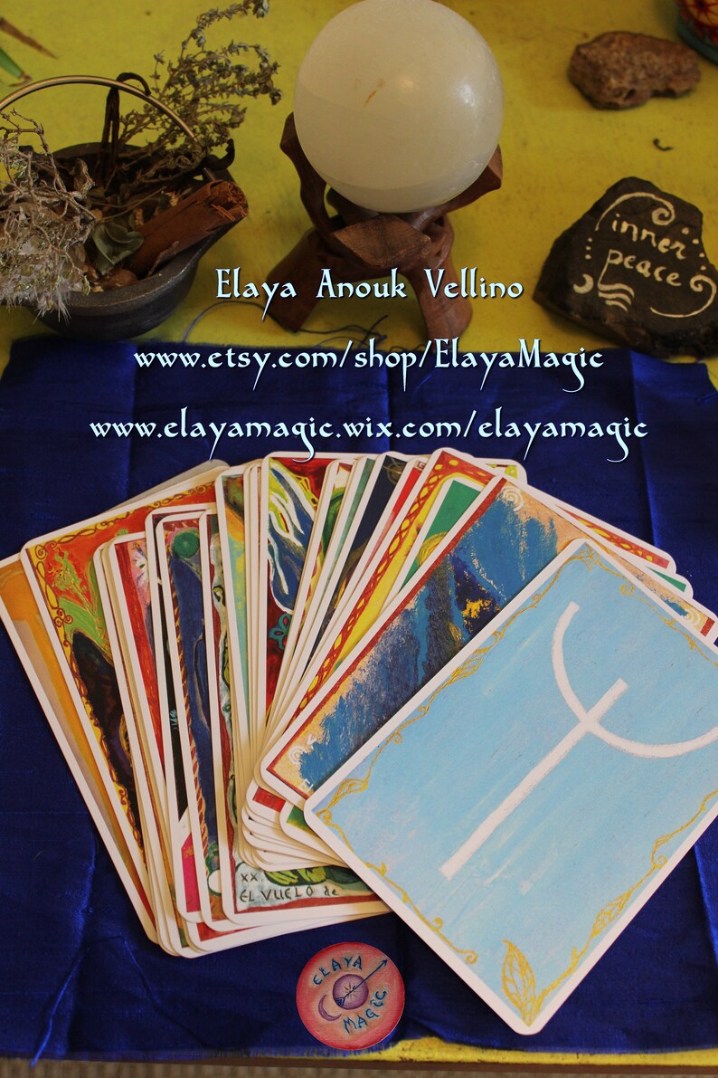 May include: A deck of tarot cards with colorful illustrations and gold trim. The cards are fanned out on a blue surface. The top card shows a white symbol on a blue background. The text "inner peace" is written on a black stone in the background. The text "Elaya Anouk Vellino" is written in blue on a white background. The text "www.etsy.com/shop/ElayaMagic" is written in blue on a white background. The text "www.elayamagic.wix.com/elayamagic" is written in blue on a white background.