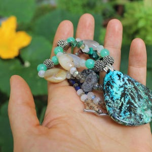 Peut inclure: Un collier avec un pendentif en pierre turquoise et noire, avec des perles vertes et blanches. Le collier est fait de pierres naturelles et comporte un fermoir argenté.