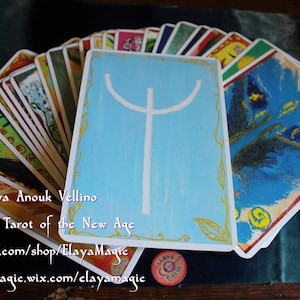 May include: A spread of cards from the Elven Tarot of the New Age deck by Elaya Anouk Vellino. The cards feature colorful illustrations and a blue card with a white symbol in the center.