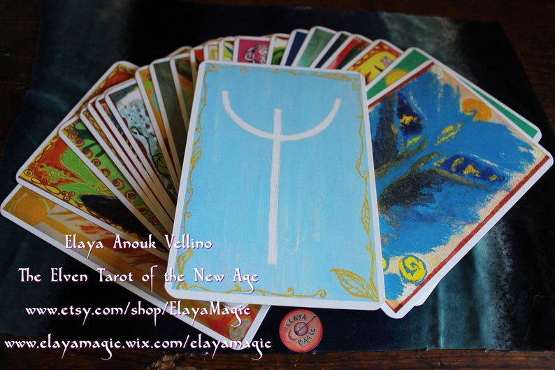 May include: A spread of cards from the Elven Tarot of the New Age deck by Elaya Anouk Vellino. The cards feature colorful illustrations and a blue card with a white symbol in the center.