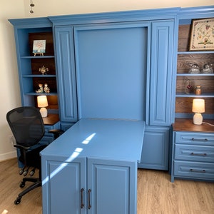 Pu&ograve; includere: Un'unit&agrave; a muro blu con una scrivania a scomparsa e mensole. La scrivania &egrave; in legno e ha una finitura blu chiaro. Le mensole sono in legno e hanno una finitura marrone scuro. C'&egrave; una sedia da ufficio nera davanti alla scrivania.
