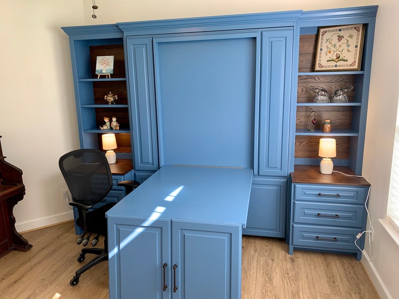 Pu&ograve; includere: Un'unit&agrave; a muro blu con una scrivania a scomparsa e mensole. La scrivania &egrave; in legno e ha una finitura blu chiaro. Le mensole sono in legno e hanno una finitura marrone scuro. C'&egrave; una sedia da ufficio nera davanti alla scrivania.