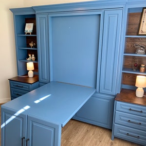 Pu&ograve; includere: Un'unit&agrave; a muro blu con un letto a scomparsa e una scrivania. L'unit&agrave; ha mensole e armadi, e la scrivania &egrave; in legno. Ci sono due lampade sull'unit&agrave;, una su ogni lato della scrivania.