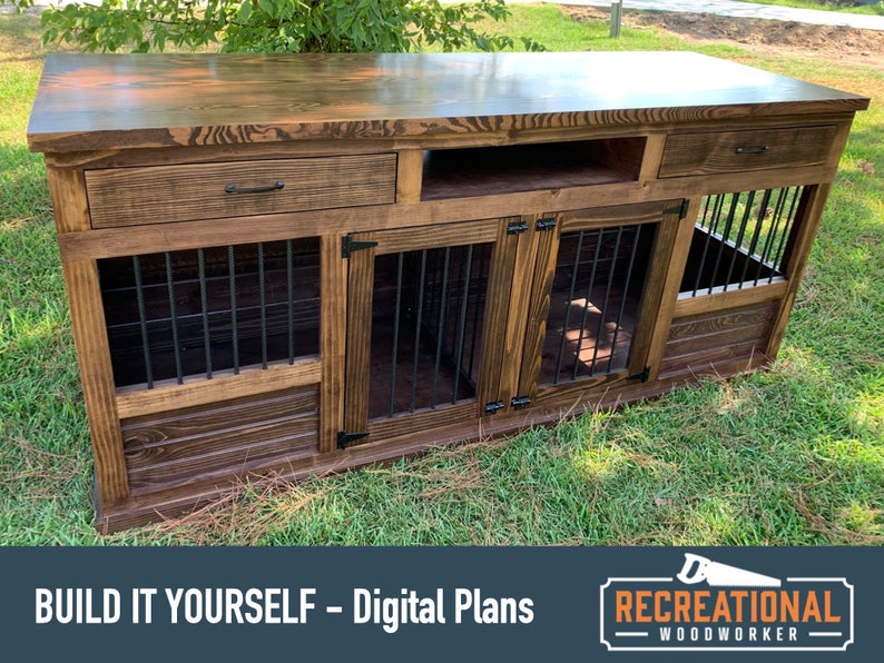 May include: A wooden dog crate with two separate compartments, a top shelf, and two drawers. The crate is stained a dark brown color and has black metal bars on the front of each compartment. The crate is sitting on a green grassy lawn. "BUILD IT YOURSELF - Digital Plans" and "RECREATIONAL WOODWORKER" are printed on the bottom of the image.