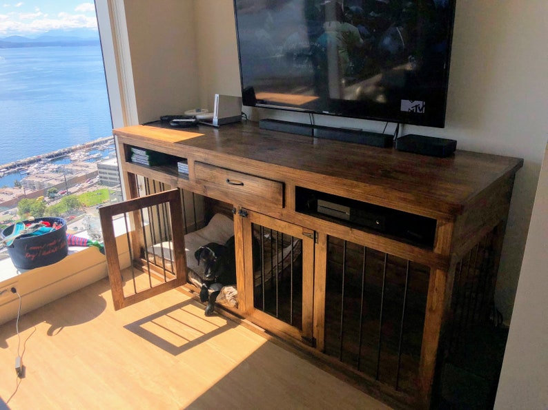 May include: A wooden entertainment center with a built-in dog crate. The crate has a door that is open and a black dog is inside. The entertainment center has a drawer and shelves.