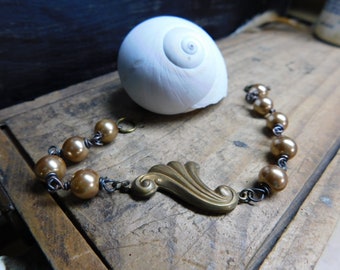 May include: A gold-toned bracelet with a decorative brass charm and brown beads. The bracelet is made with wire and beads.