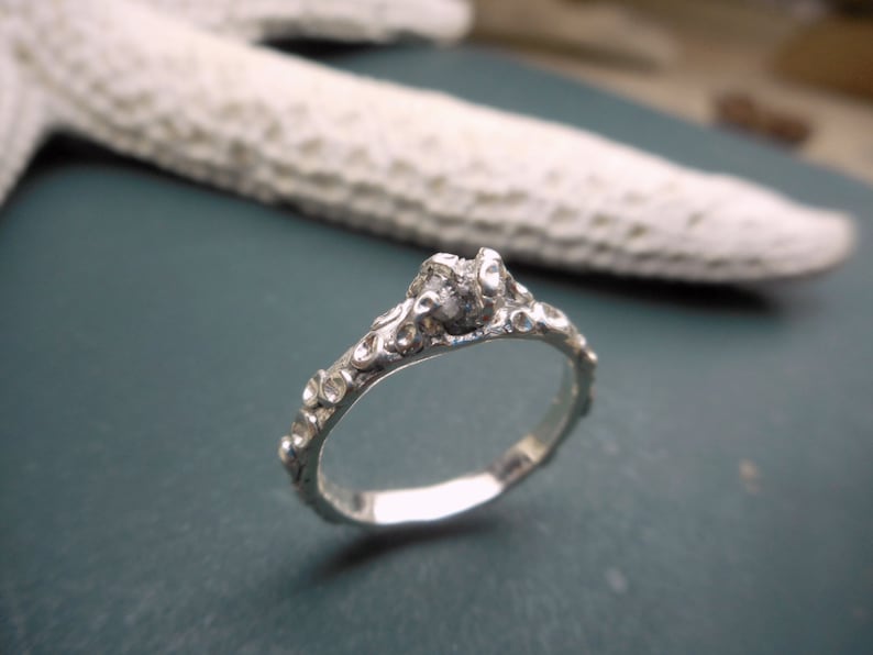 May include: A silver ring with a textured, organic design. The ring features a single, small, clear gemstone.