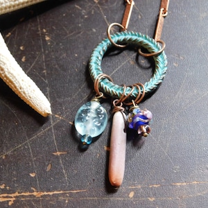 May include: A turquoise and copper wire wrapped pendant necklace with a variety of glass beads, including a light blue teardrop bead, a pink and white bead, and a blue and purple bead.