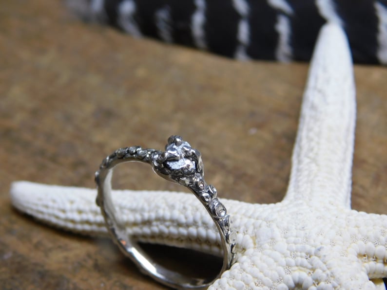 May include: A silver ring with a textured, organic design. The ring is set against a white starfish background.