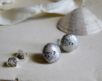 May include: A pair of silver earrings shaped like sea urchins. The earrings have a textured surface and a small hole in the center.
