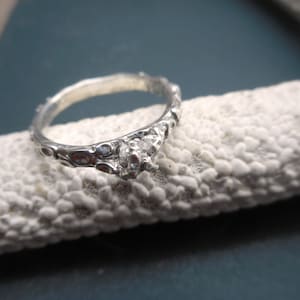 May include: A silver ring with a textured band and a single clear stone set in the center.