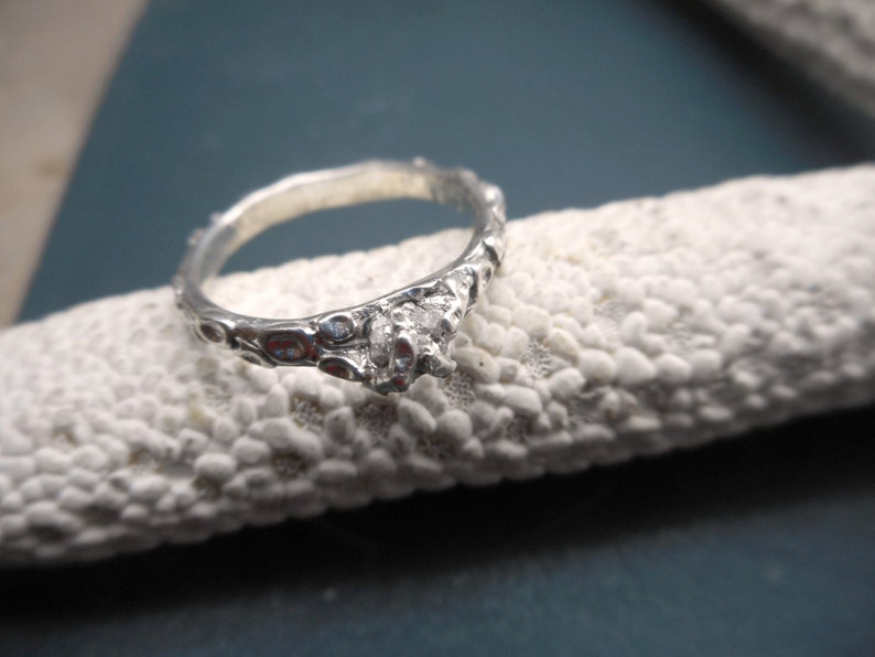 May include: A silver ring with a textured band and a single clear stone set in the center.