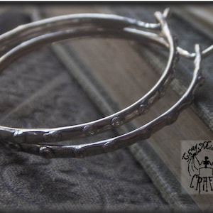 May include: A pair of silver hoop earrings with a textured, twig-like design.