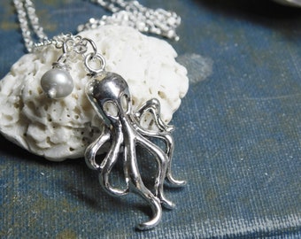 May include: Silver octopus pendant necklace with a white pearl charm. The necklace is on a white coral-like surface.