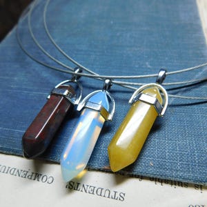 May include: Three silver chain necklaces with different colored crystal pendants. The pendants are shaped like long, pointed crystals. The crystals are red, white, and yellow.