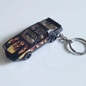 May include: Black toy car keychain with yellow and red flame decals. The miniature car has a clear roof and silver keychain ring. The car's wheels are black with silver rims. A fun accessory for car enthusiasts.