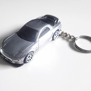 May include: A silver toy car keychain with a silver key ring. The car is a sports car with a spoiler and black wheels.