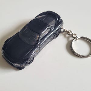 Puede incluir: Llavero de coche negro con un llavero plateado. El coche es una réplica detallada de un coche deportivo.