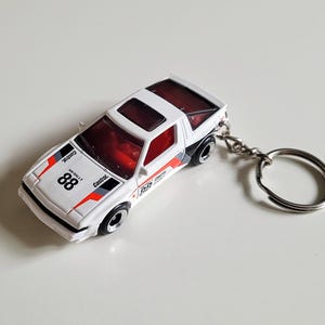 May include: A white and red toy car keyring with the number 88 and the word "Castrol" printed on it. The car has black wheels and a silver key ring. The car's interior is red.