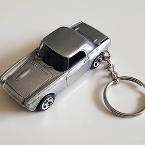 Pode incluir: Um chaveiro de carro de brinquedo prateado com um modelo clássico Honda S600. O carro tem um interior preto e um chaveiro prateado.