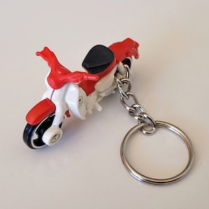 May include: Red and white motorcycle keychain with a black seat and a silver chain.
