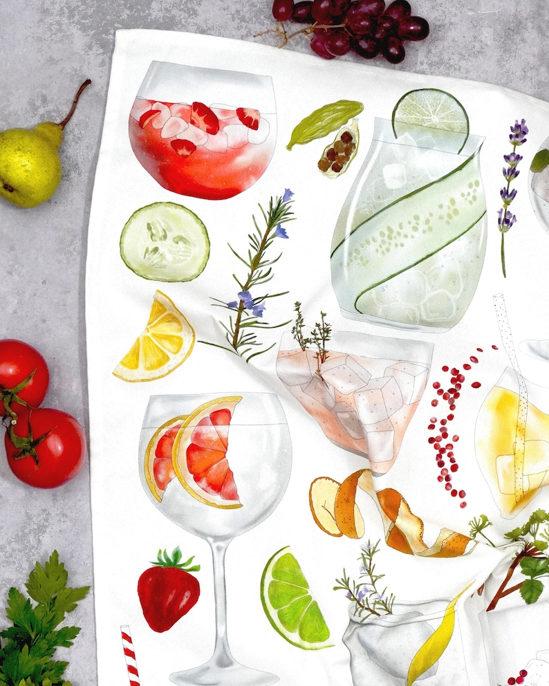 May include: A white kitchen towel with watercolor illustrations of various gin and tonic ingredients, including lime wedges, cucumber slices, grapefruit, rosemary sprigs, and peppercorns.