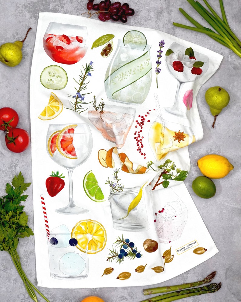 May include: White kitchen towel with a colorful illustration of various ingredients and cocktails. The illustration includes lemons, limes, berries, herbs, and ice. The text "Corinne Alexander" is printed in the bottom right corner.