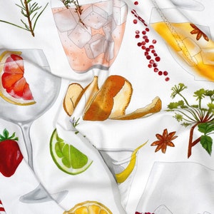 May include: A white tea towel with a colorful pattern of various fruits, herbs, and spices. The pattern includes a grapefruit, lime, orange, star anise, rosemary, thyme, and a peeled pear. There are also several glasses of pink and yellow drinks with ice cubes.