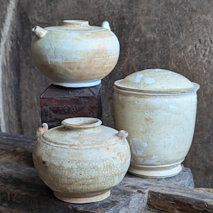 Pode incluir: Três vasos de cerâmica com acabamento em esmalte craquelado. Os vasos são em tons de branco e bege. Os vasos estão dispostos sobre uma superfície de madeira.