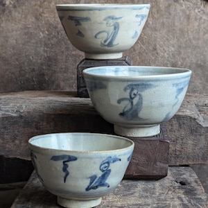 Puede incluir: Tres cuencos de cerámica blanca con diseños florales azules y blancos. Los cuencos están apilados uno encima del otro, con el cuenco más grande en la parte inferior y el más pequeño en la parte superior.