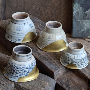 Peut inclure: Quatre petits bols en céramique blanche avec des motifs bleus et dorés. Les bols ont une forme arrondie et un bord large. Le bord doré est à l'extérieur du bol.