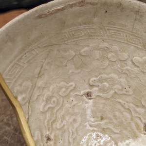 Könnte beinhalten: Nahaufnahme einer weißen Keramikschale mit craquelé-Glasur. Die Schale hat ein dekoratives Design aus stilisierten Wolken und einem Rand aus sich wiederholenden geometrischen Mustern.