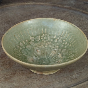 May include: A green ceramic bowl with a floral design. The bowl has a wide rim and a rounded base.