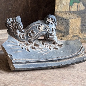 Może przedstawiać: Czarny atramentarz ceramiczny z wzorem smoka. Atramentarz jest pęknięty i ma szorstką, fakturowaną powierzchnię.