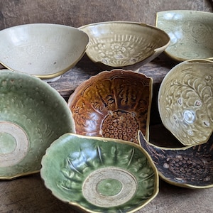 Puede incluir: Una colección de siete cuencos de cerámica antiguos con diversos diseños y colores. Los cuencos están hechos de cerámica vidriada y tienen una variedad de patrones, incluyendo diseños florales, geométricos y abstractos. Los cuencos están en varios estados de desgaste, algunos muestran signos de edad y uso.