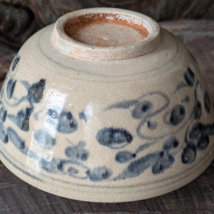 Peut inclure: Bol en céramique vintage avec une base crème et des motifs floraux bleus. Le bol a une forme légèrement évasée et un glaçage craquelé visible. Le bord est brun rougeâtre, et le bol semble ancien.